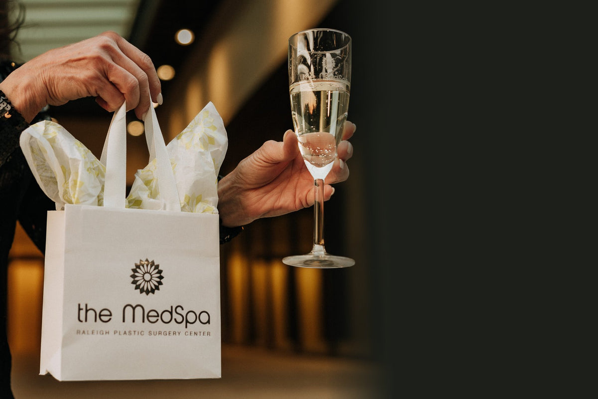 A guest holding a The MedSpa gift bag and a glass of champagne at Shineslider_item_shine2026